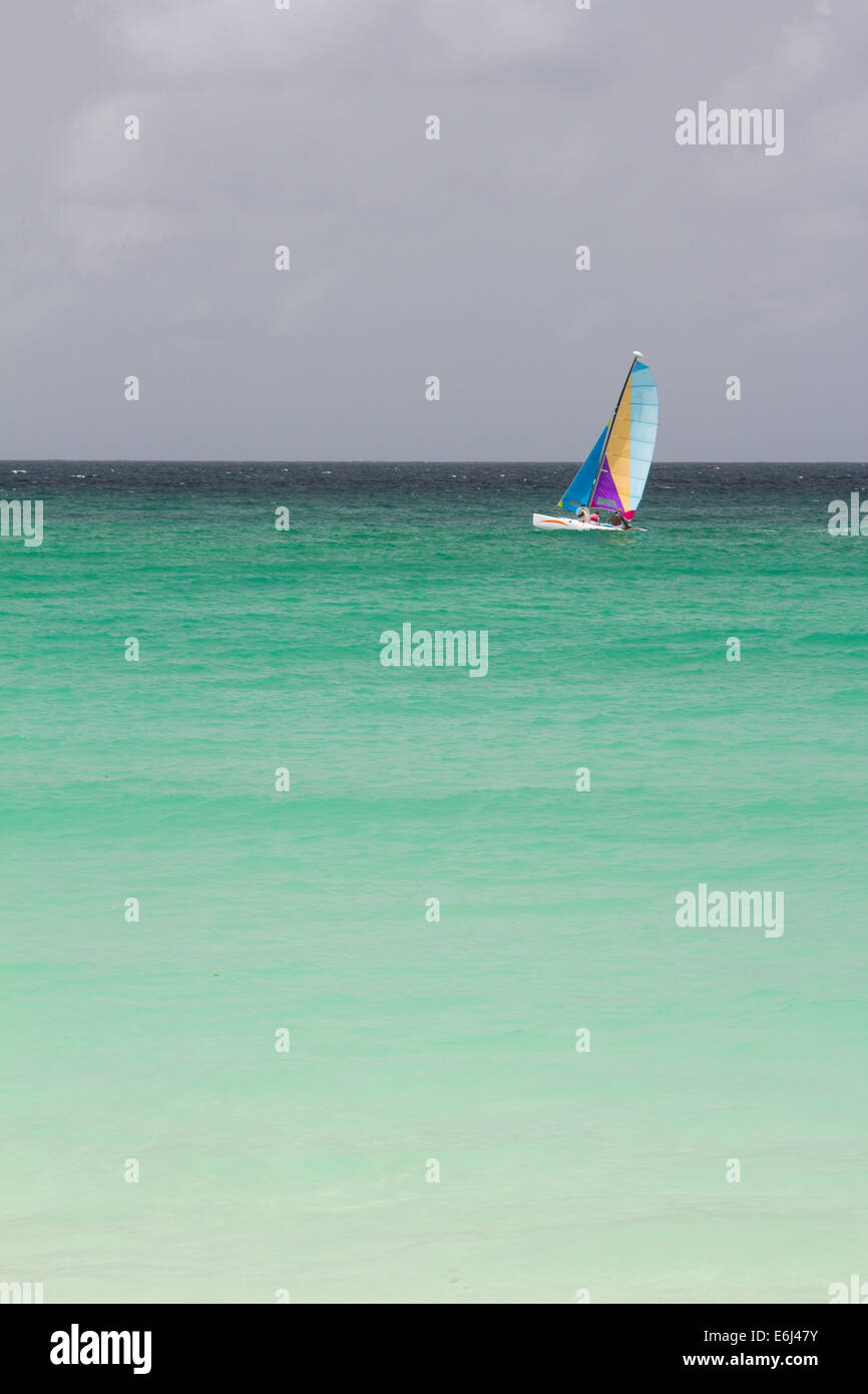 Barca a vela su un mare turchese contro un oscuro moody sky in Barbados Foto Stock