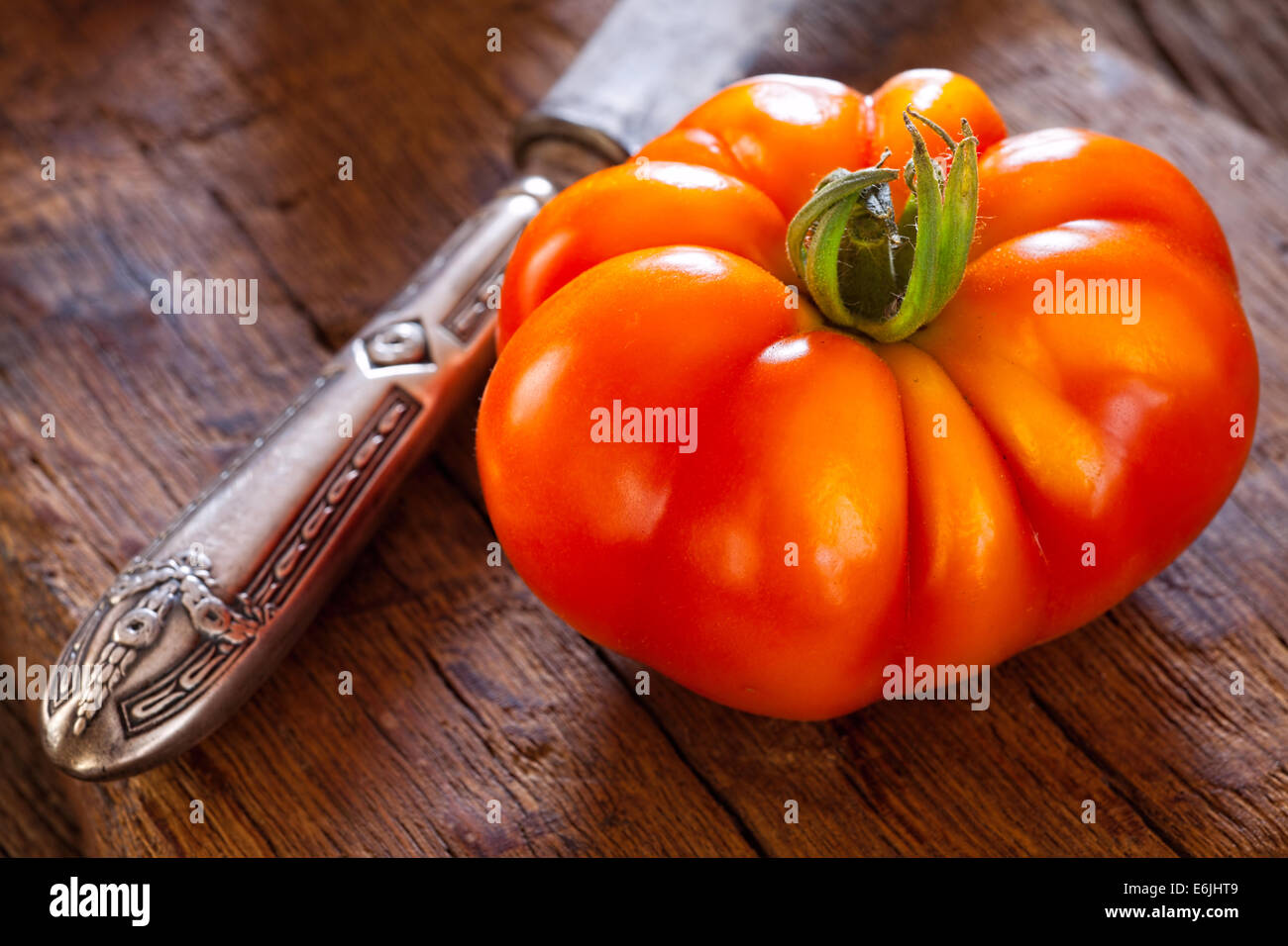 Close up di un maturo bistecca di manzo pomodoro dal proprio giardino e un coltello da tavola su un rustico tagliere in stile country Foto Stock
