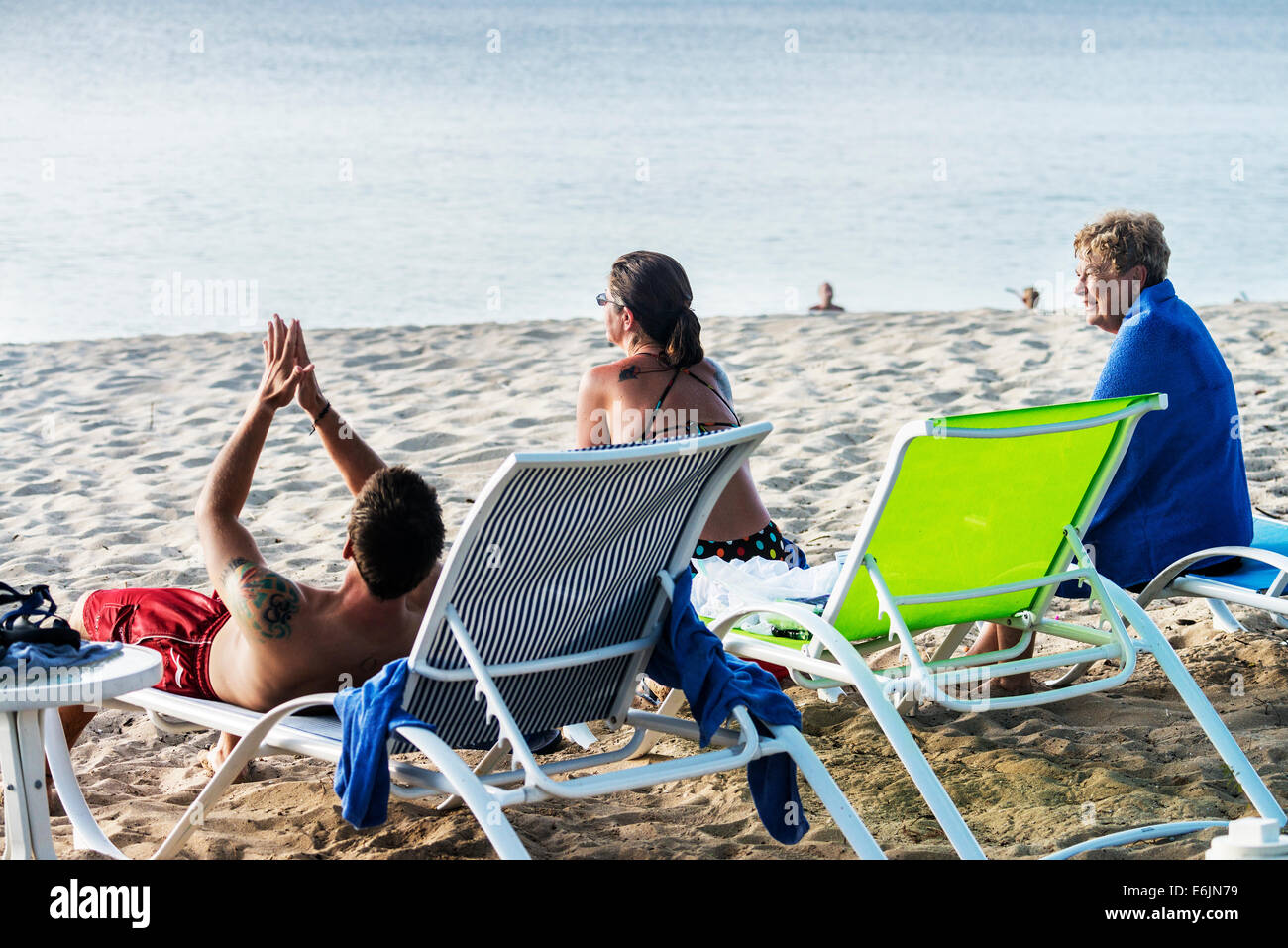Tre persone conversare e godere di una spiaggia tropicale mentre vi rilassate sulle sedie a sdraio. Foto Stock