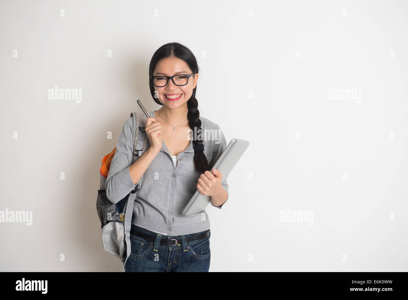 Asian college girl pensando tenendo la penna con il computer portatile su sfondo semplice Foto Stock