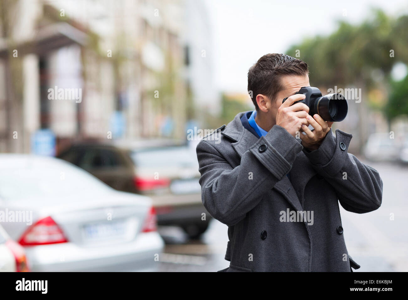 Giovane fotografo scatta le foto sulla strada di città sotto la pioggia Foto Stock