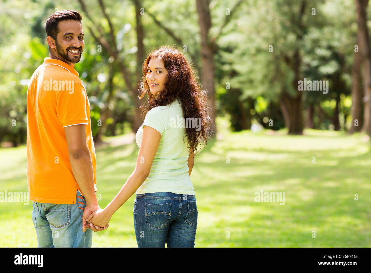 Carino coppia indiano tenendo le mani e guardando indietro all'aperto Foto Stock
