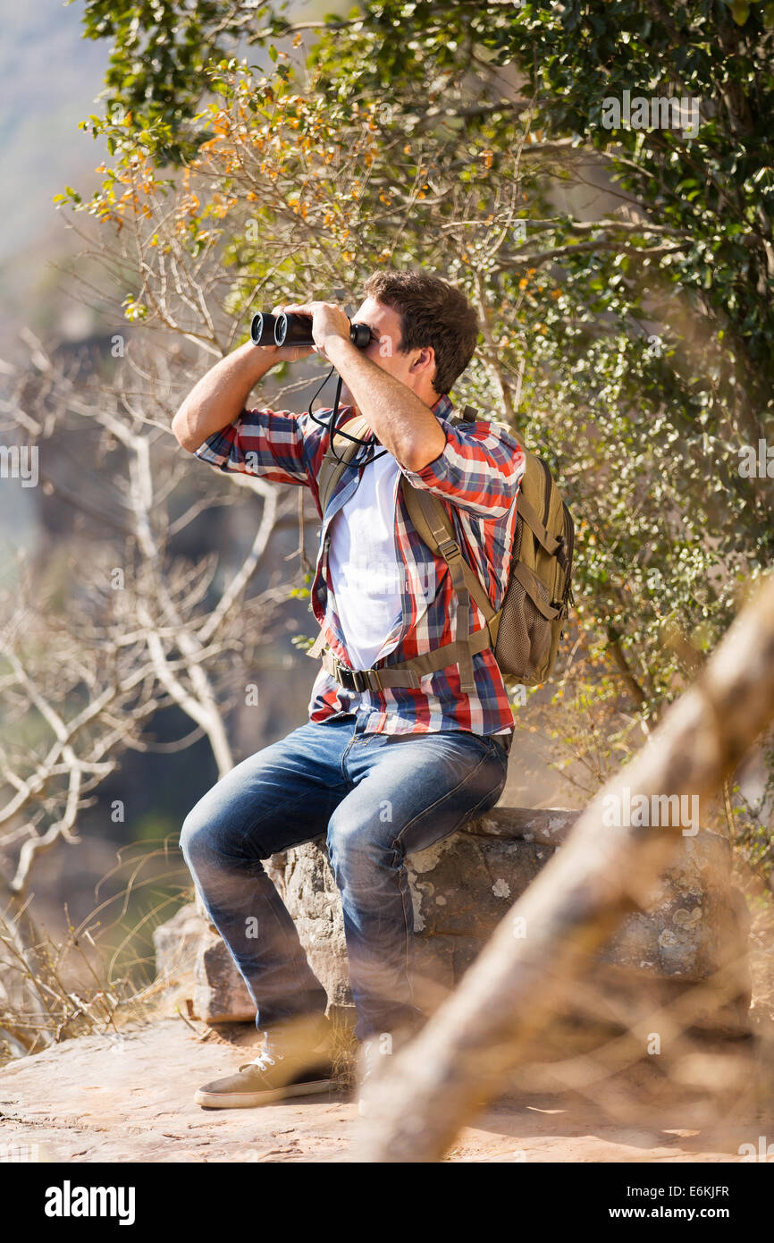 Giovane uomo seduto sulla cima della montagna e utilizzando il binocolo Foto Stock