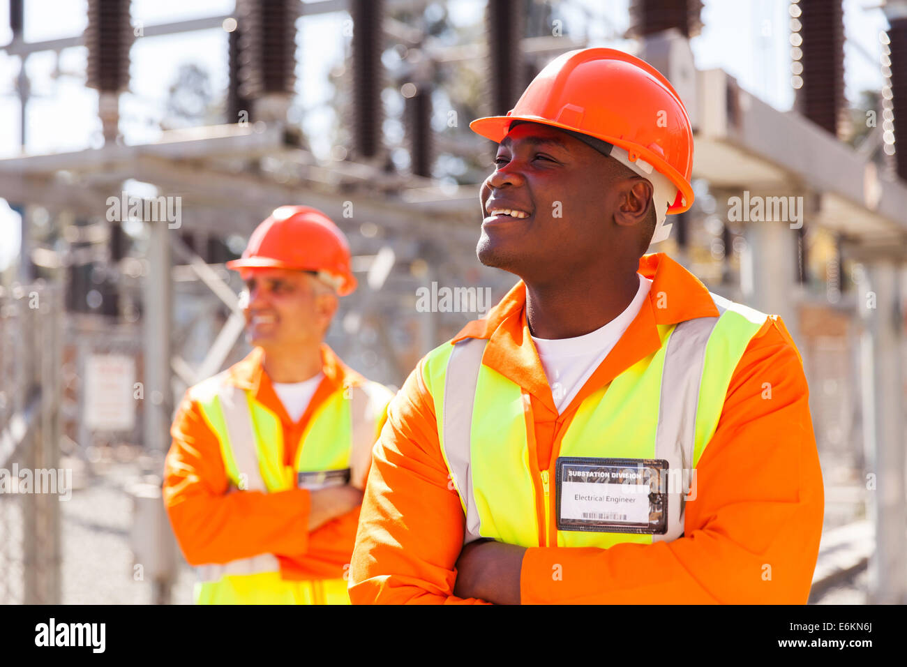 Sorridente africana di ingegnere elettrico nella sottostazione con il collega in background Foto Stock