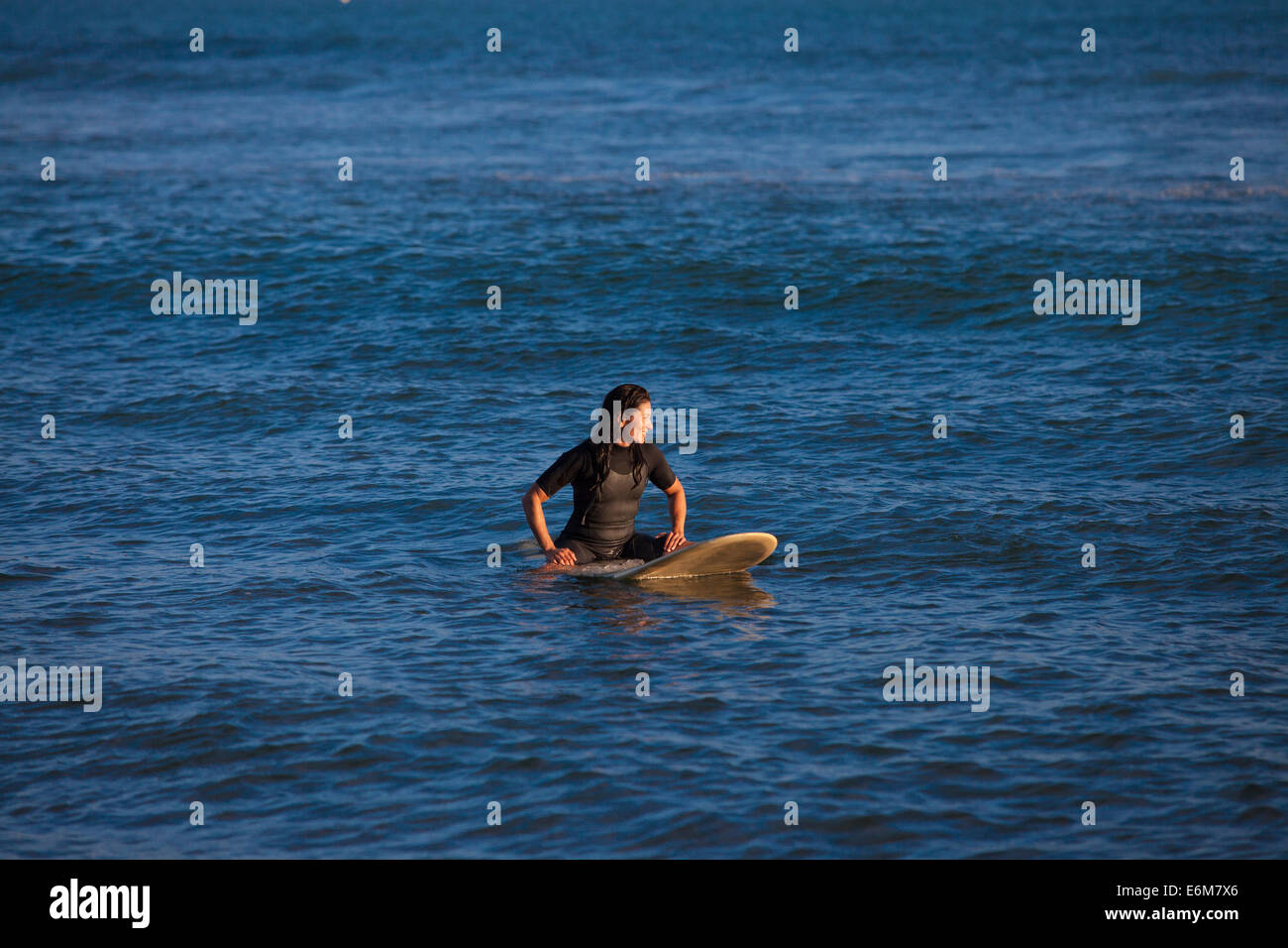 Donna seduta sulla tavola da surf galleggiante sull'acqua Foto Stock