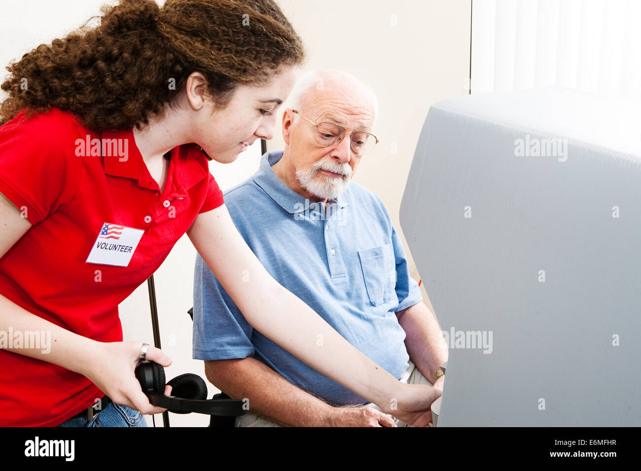 Elezione Teenage volontario aiuta i non udenti senior uomo usare il touch screen e le cuffie. Foto Stock