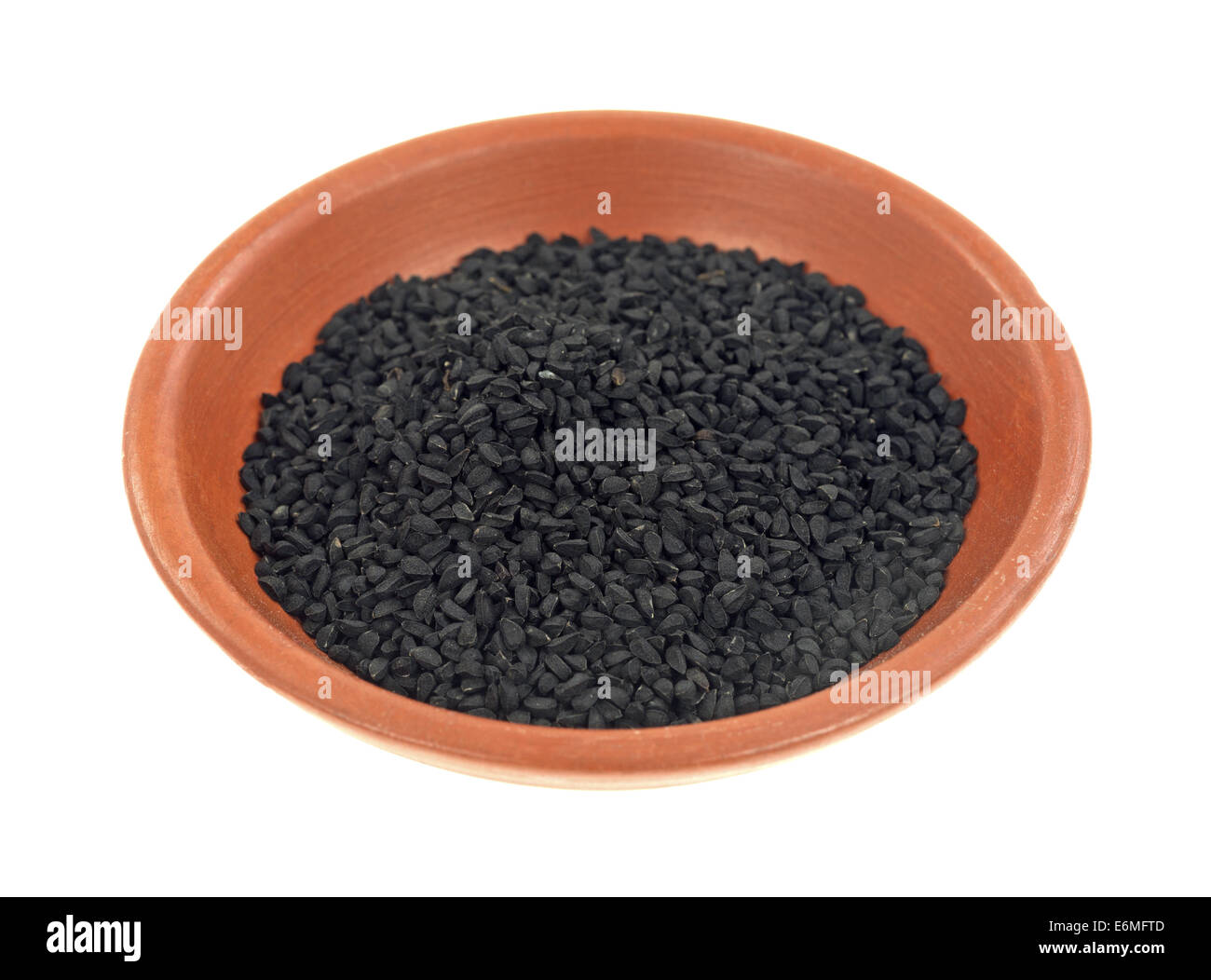 Una piccola ciotola di argilla con una porzione di nero semi di cumino su uno sfondo bianco. Foto Stock