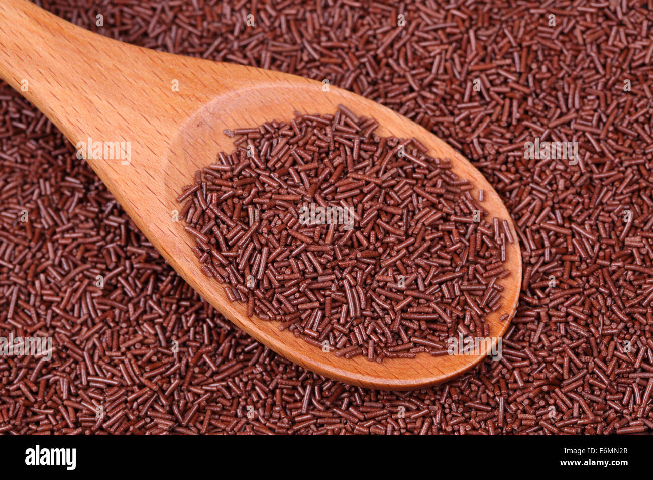 Gocce di cioccolato in un cucchiaio di legno su scaglie di cioccolato sfondo. Primo piano. Foto Stock