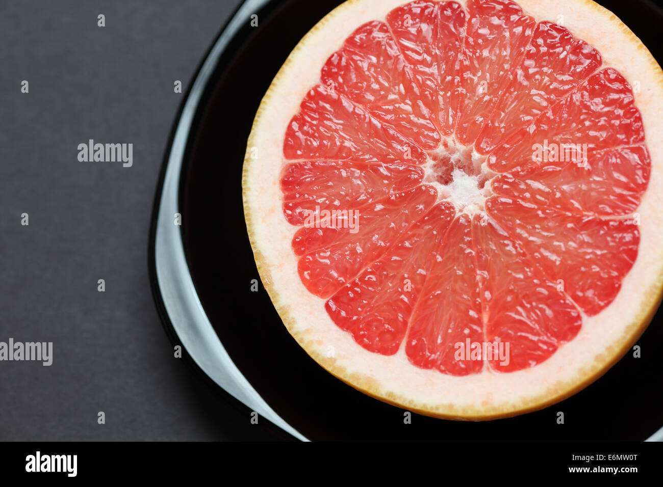 Semi di fresco pompelmo rosso in una piastra nera su sfondo nero. Primo piano. Foto Stock