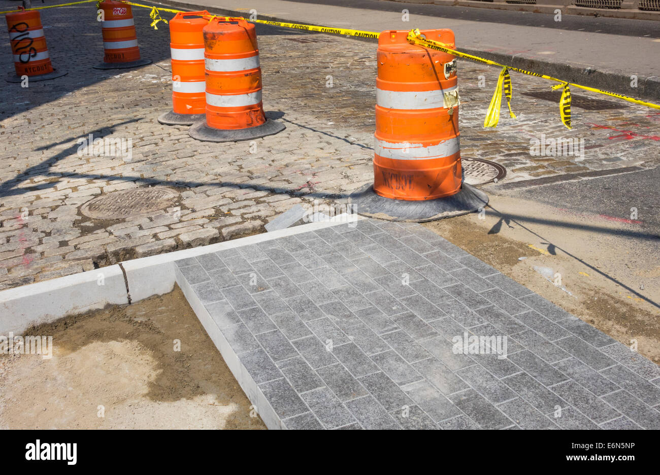 Pronte le pietre per pavimentazione la sostituzione di blocchi belga nella riparazione di una strada di Soho a New York città protetta dai tamburi del traffico Foto Stock