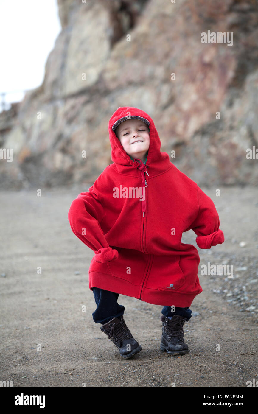 ragazzino bianco vestito con una felpa rossa di dimensioni maggiori, con divertenti rughe e balli in montagna Foto Stock