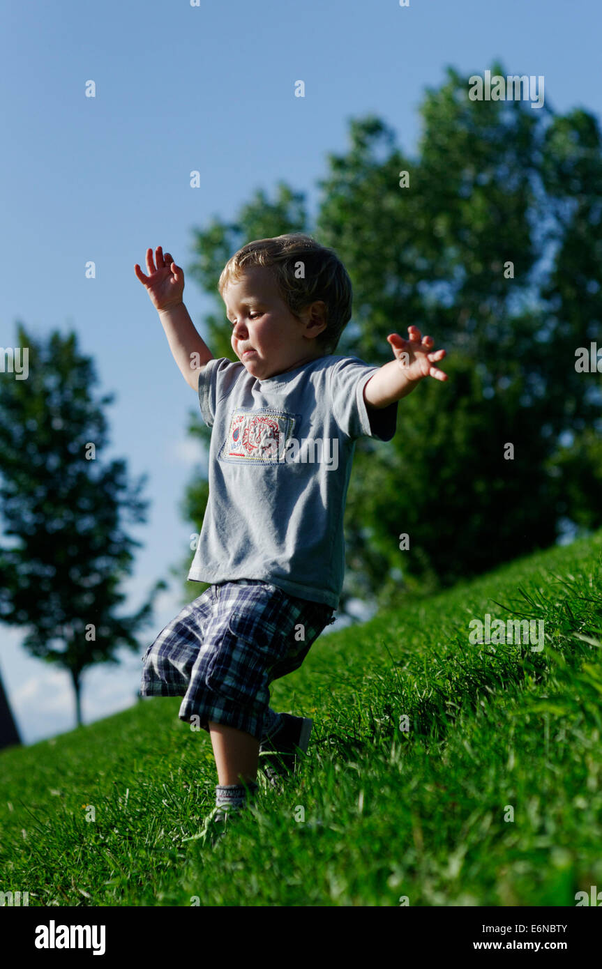 Un giovane ragazzo che corre lungo un pendio erboso Foto Stock