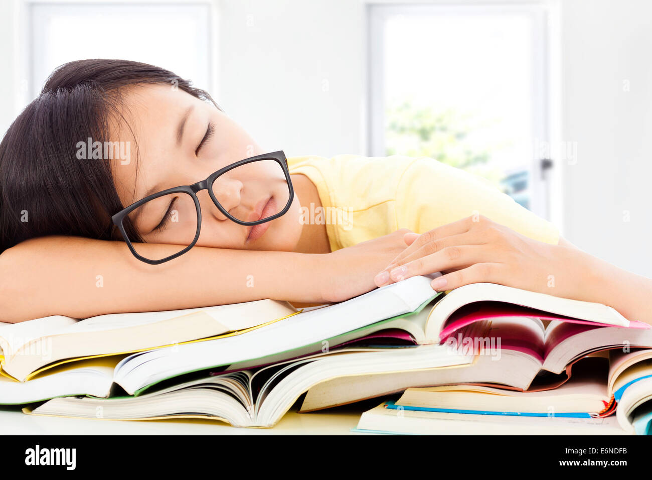 Stanco studente ragazza con gli occhiali dormire sui libri con sfondo in camera Foto Stock