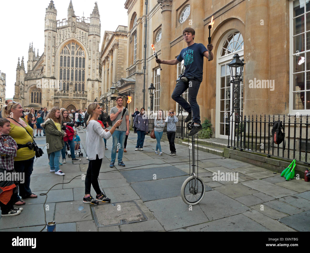 Street performer giocoleria con il fuoco su un monociclo guardato da turisti al di fuori Abbazia di Bath Bath, Inghilterra KATHY DEWITT Foto Stock