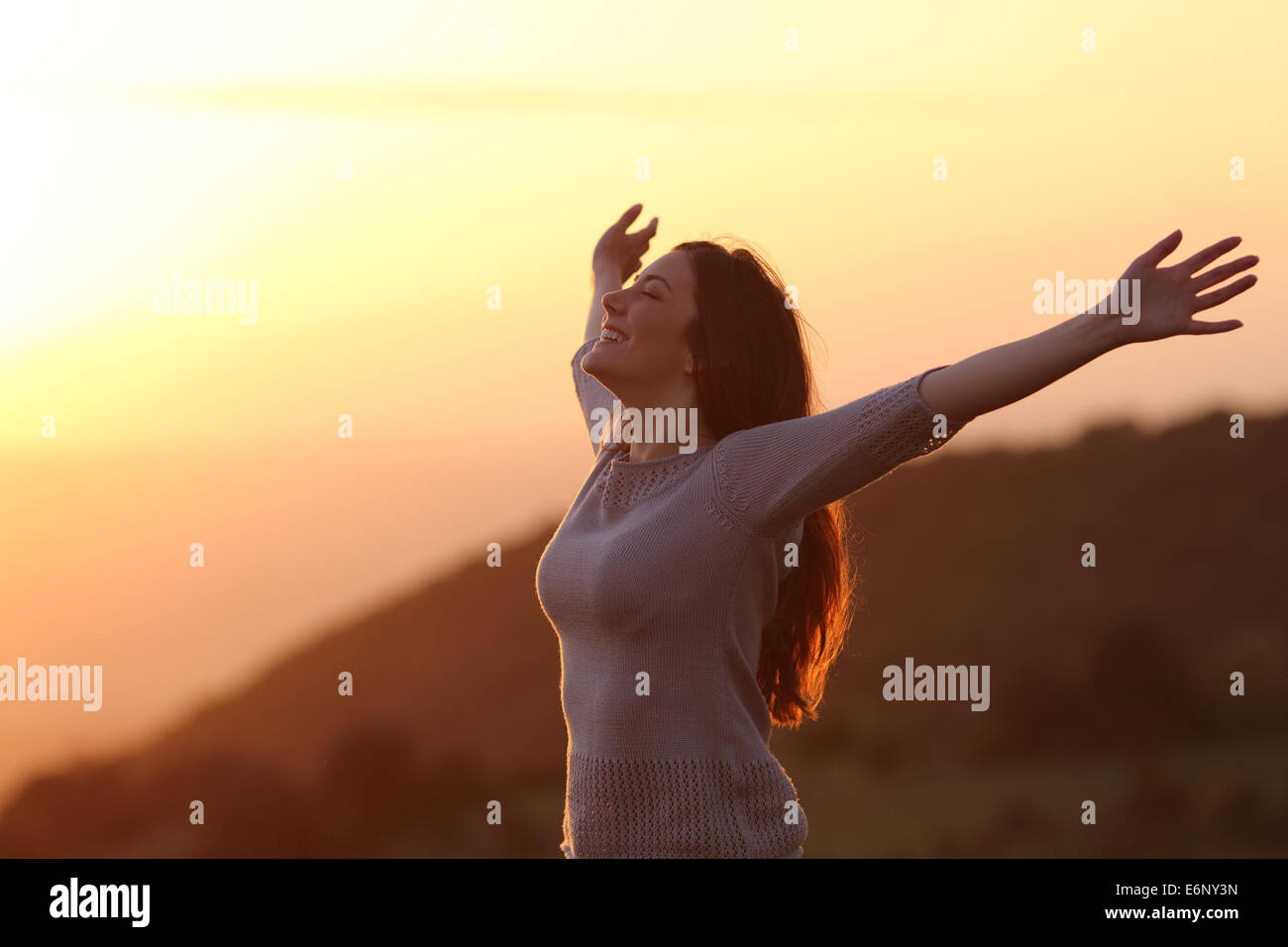 Retroilluminazione del una donna al tramonto respirando aria fresca dei bracci di sollevamento Foto Stock