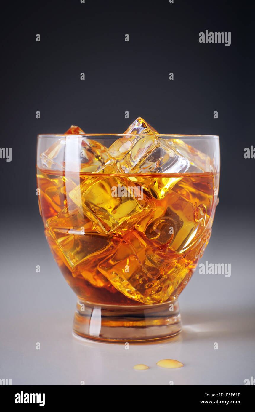 La bevanda alcolica in un bicchiere con cubetti di ghiaccio e la fuoriuscita di gocce sul tavolo Foto Stock