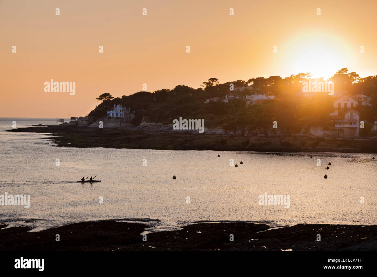 Un uomo due canoa entra nella baia di Conche de Saint Palais come il sole tramonta. Foto Stock