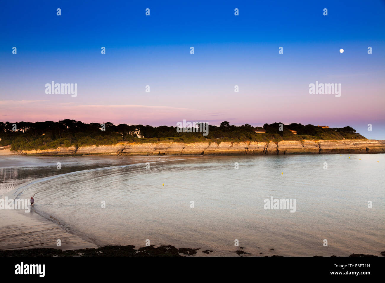 Una persona solitaria passeggiate lungo il bordo delle acque come la luna piena sorge al tramonto. Foto Stock