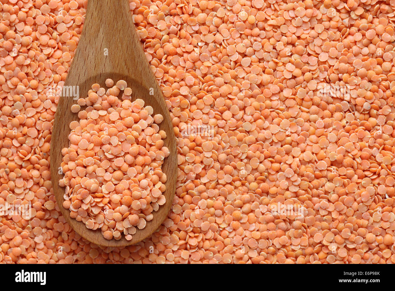 Di lenticchie rosse in un cucchiaio di legno su di lenticchie rosse sfondo. Foto Stock