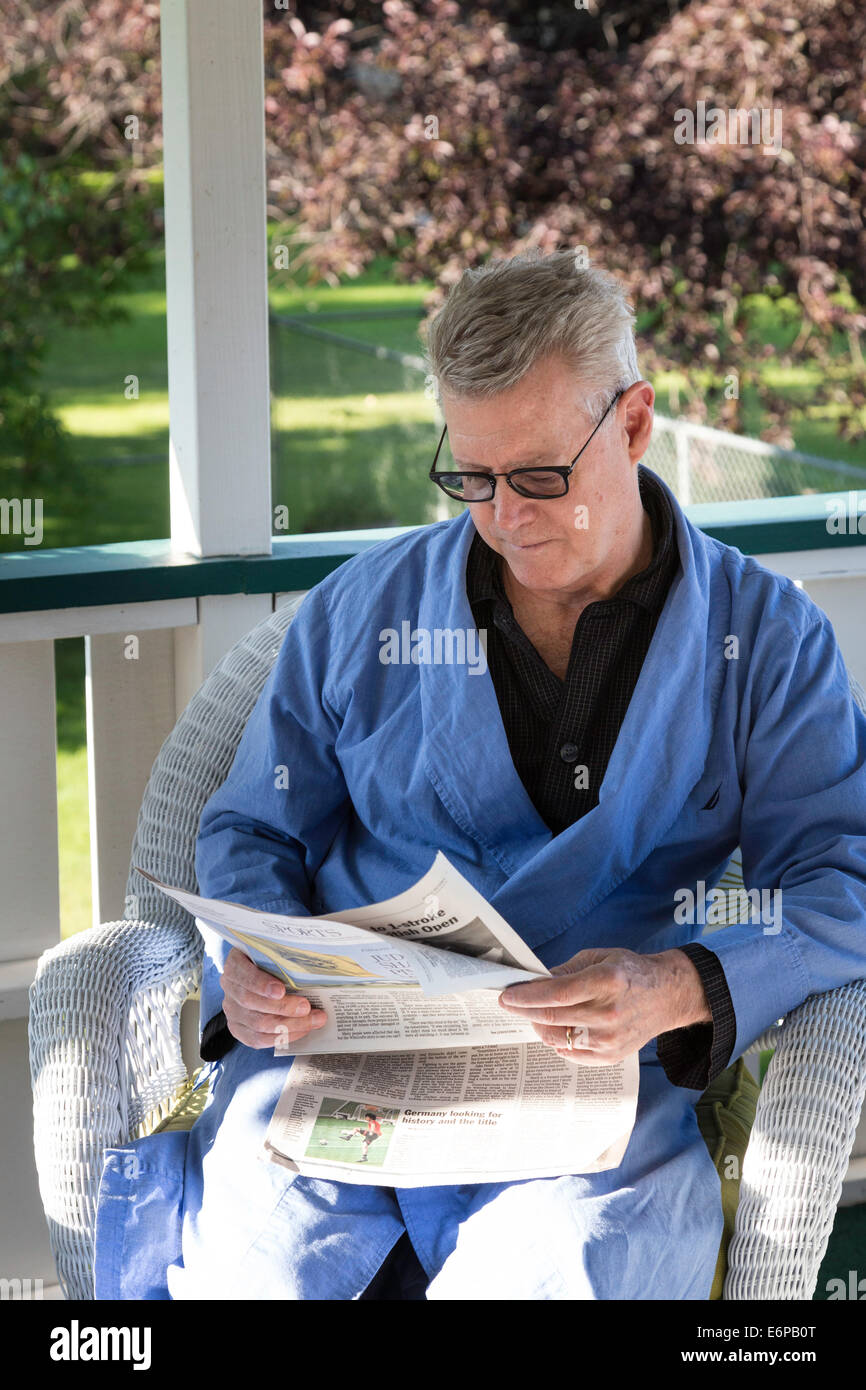 Uomo maturo sul ponte posteriore della sua casa leggere il giornale del mattino nella sua tunica e pigiami, STATI UNITI D'AMERICA Foto Stock