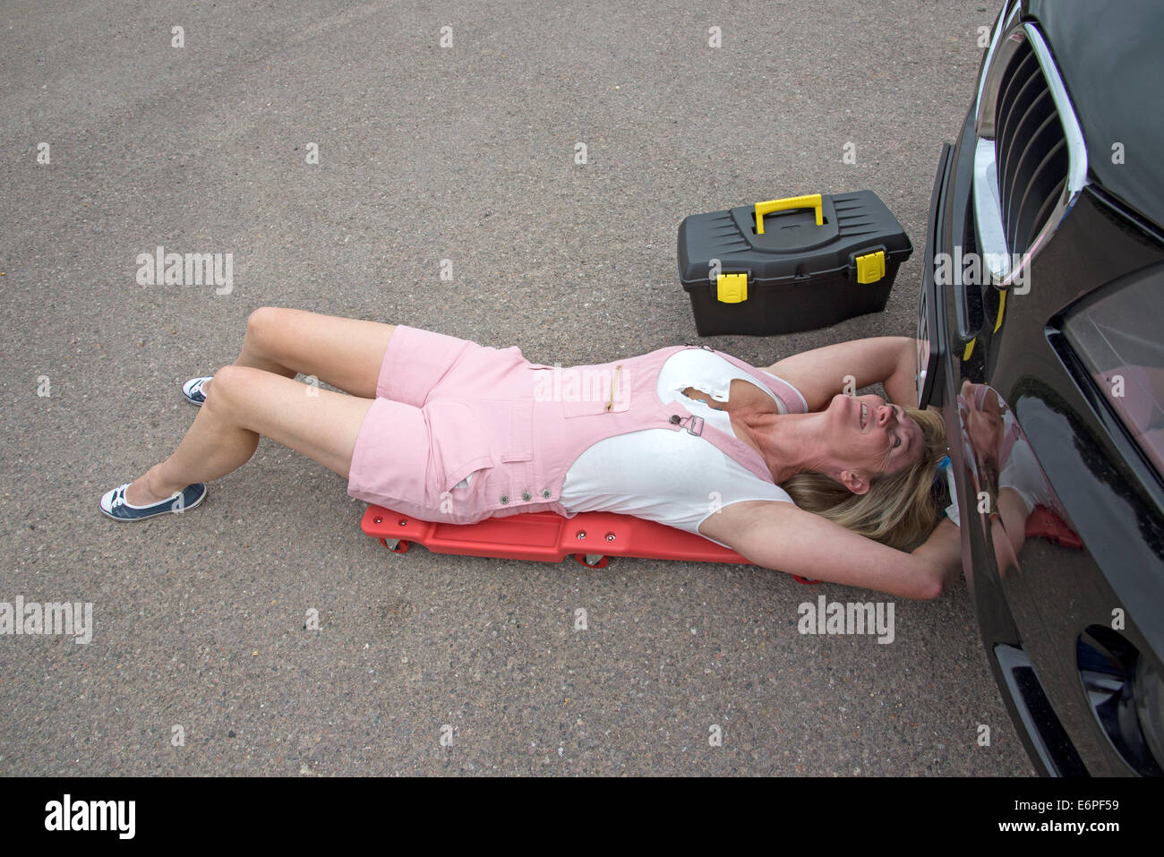Lavorando su una vettura a motore femmina meccanico posa su un cingolato per accedere al di sotto di una automobile Foto Stock