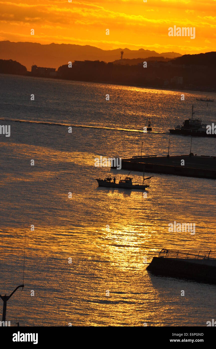 Sunrise fotografia di un piccolo porto di pescatori, una forte luce del sole dorato riflessione su increspata superficie dell'oceano Foto Stock
