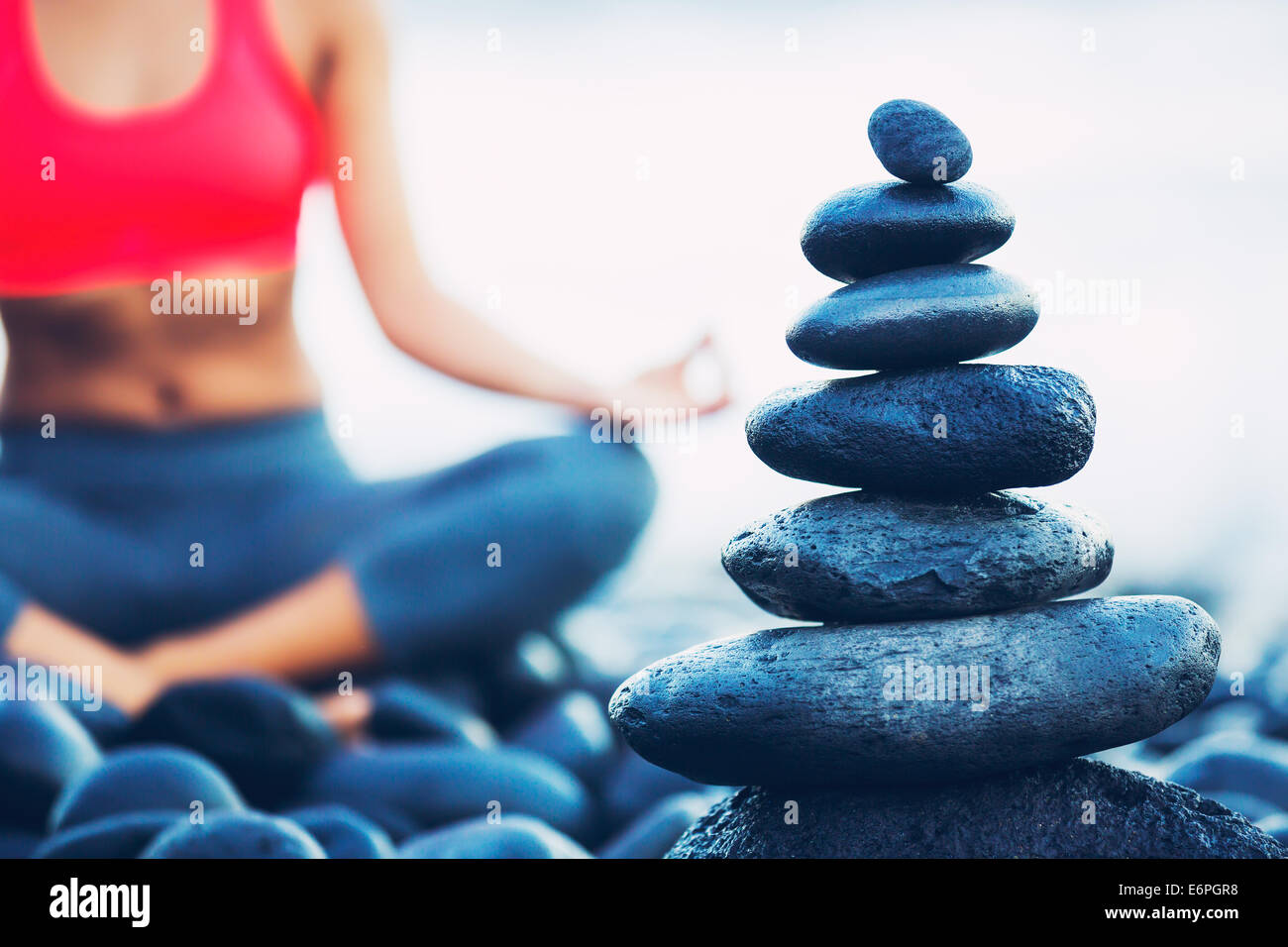 Pila di Round pietre lisce sulla riva del mare, Donna a praticare Yoga in background Foto Stock