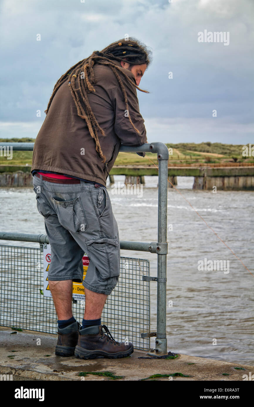 Uomo con dreadlocks appoggiato su una struttura di guardrail, Southwold Harbour, Suffolk, Regno Unito Foto Stock