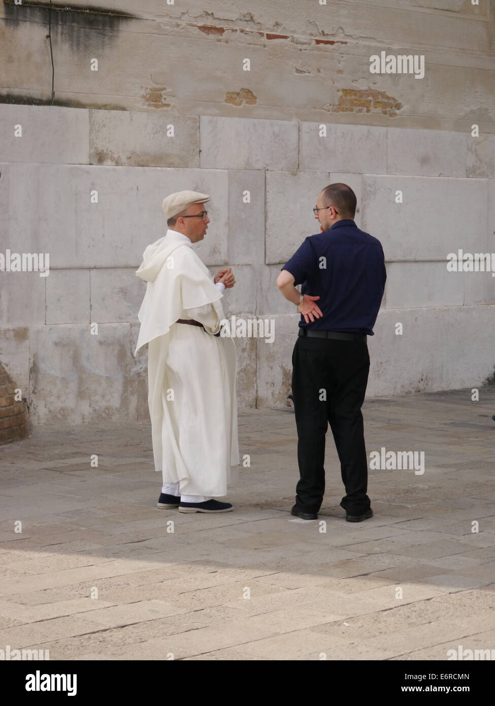 Uomo che parla al sacerdote che indossa vesti bianche in una strada di Venezia Foto Stock