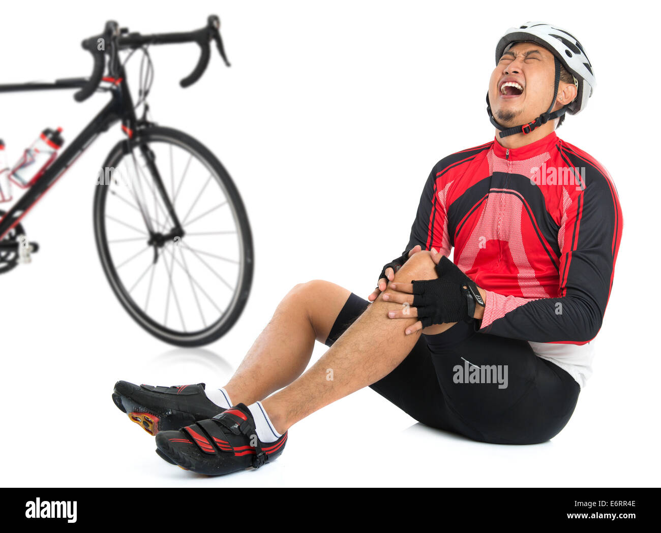 Asian ciclista è sceso dal moto con feriti del ginocchio, dolorosa espressione facciale e seduto sul pavimento, isolato su bianco bac Foto Stock