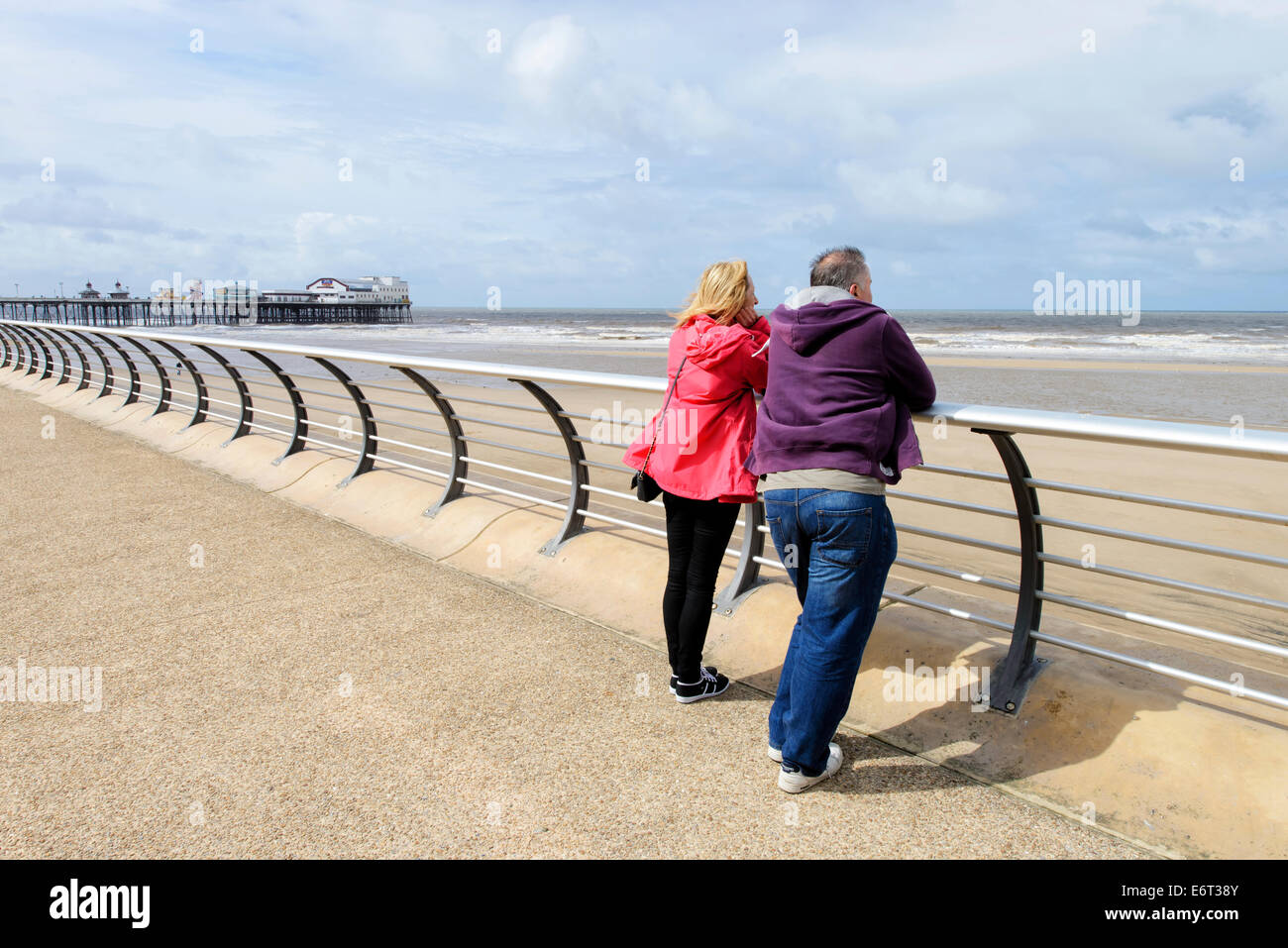 Coppia di mezza età sul lungomare di Blackpool che guarda al mare. North Pier è in background Foto Stock
