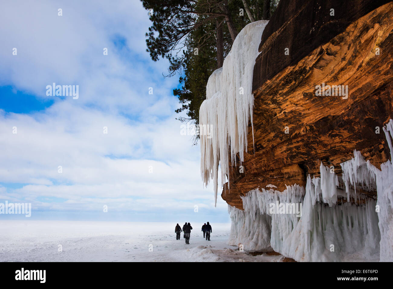 Congelati Lago Superior litorale. Arancione scogliera di pietra, grandi ghiaccioli e persone per la scala. Copia dello spazio. Apostolo Isole. Foto Stock