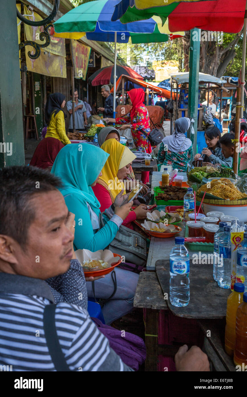 Yogyakarta, Java, Indonesia. Donne controllare i loro telefoni cellulari a un marciapiede Colazione Stand, Malioboro Street. Foto Stock