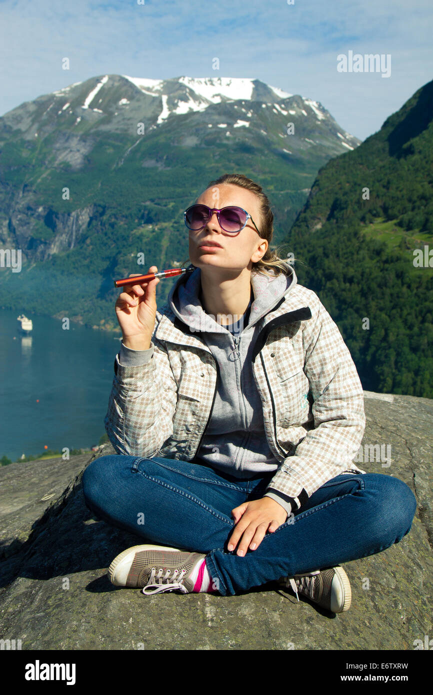 La ragazza con la sigaretta elettronica in montagna vicino al lago. instagram photo e-sigaretta Foto Stock