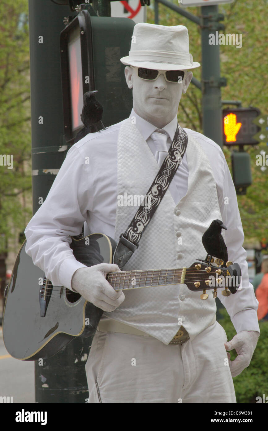 L'uomo in bianco, una statua vivente, artista di strada tutto in bianco con la chitarra e arroccata corvi, esegue per suggerimenti in Asheville NC Foto Stock