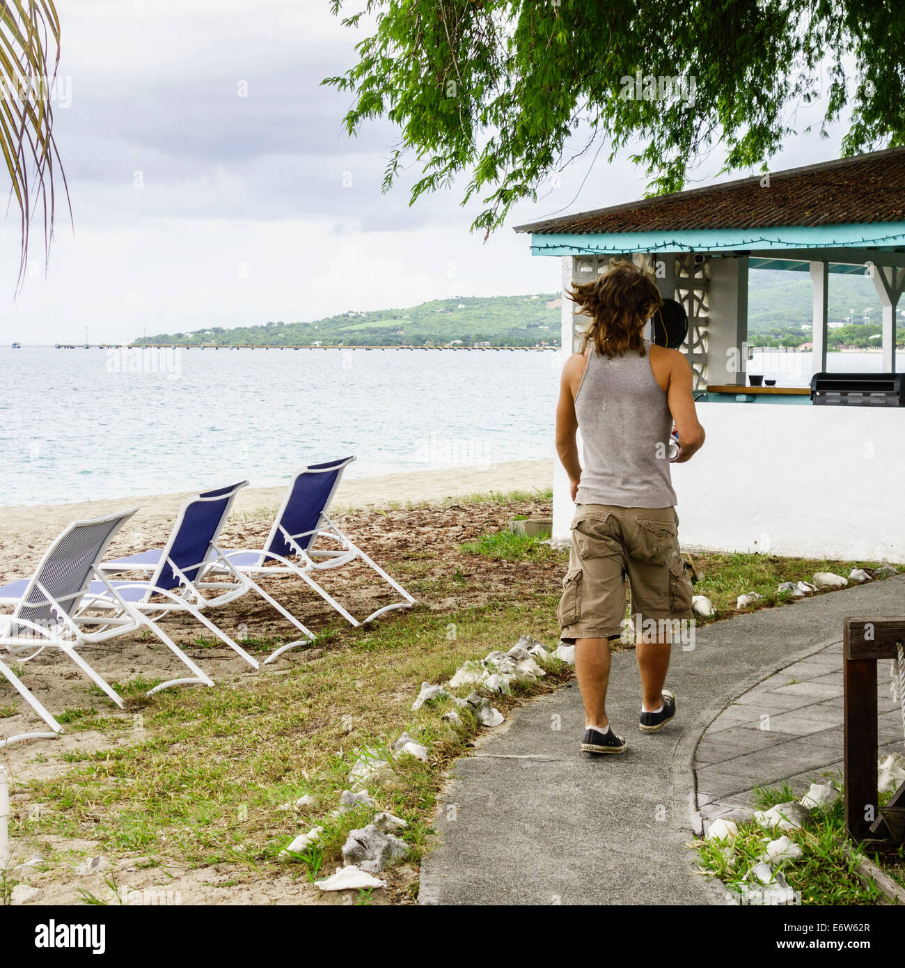 Un giovane uomo cargo in pantaloncini e maglietta muscolare passeggiate verso una cabana resort sulla spiaggia di St. Croix, U. S. Isole Vergini. Cottage sul mare resort Foto Stock