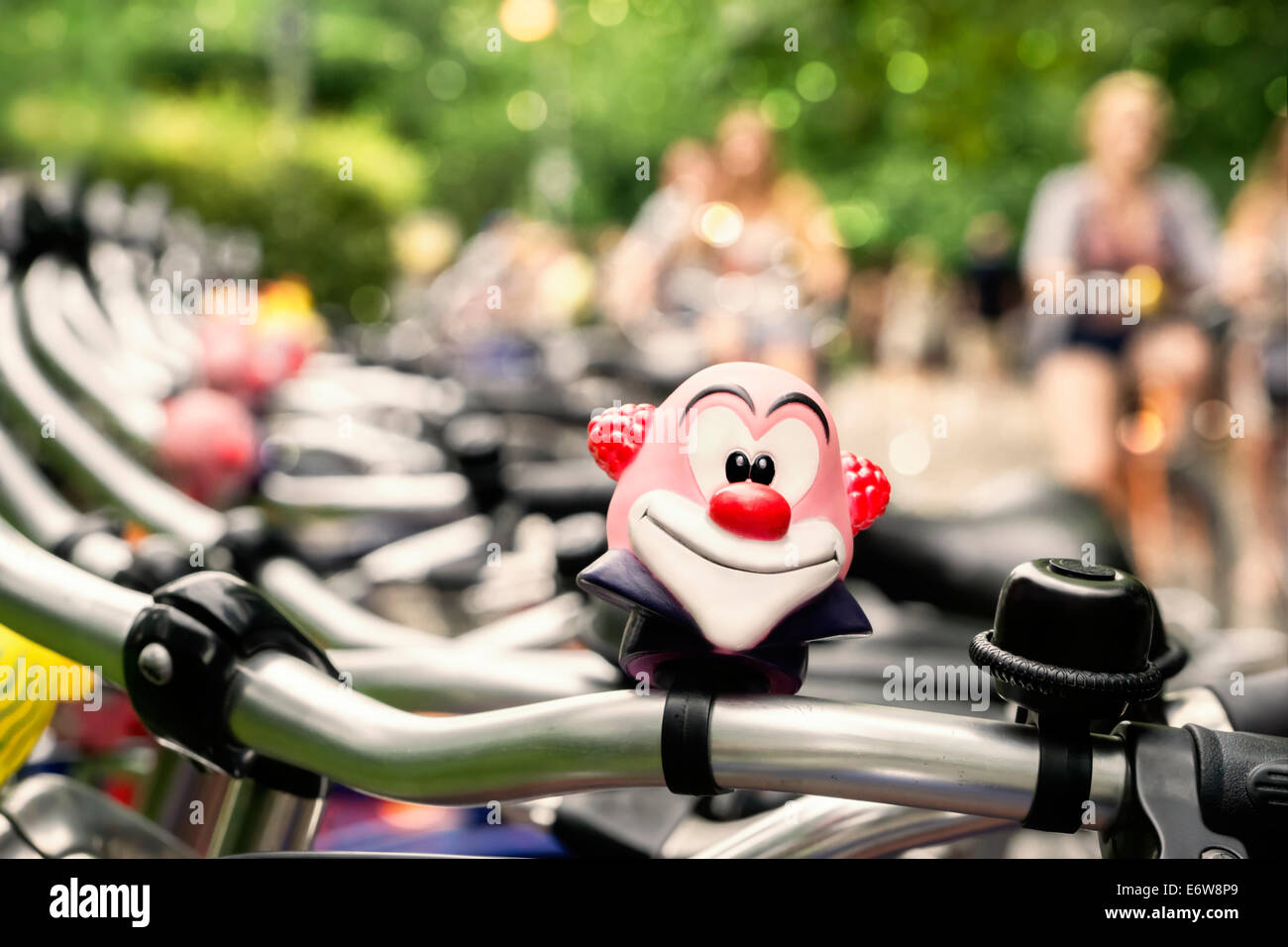 Fila di biciclette a noleggio in un parco della città con divertenti clown bell e sfocata ciclisti in background Foto Stock