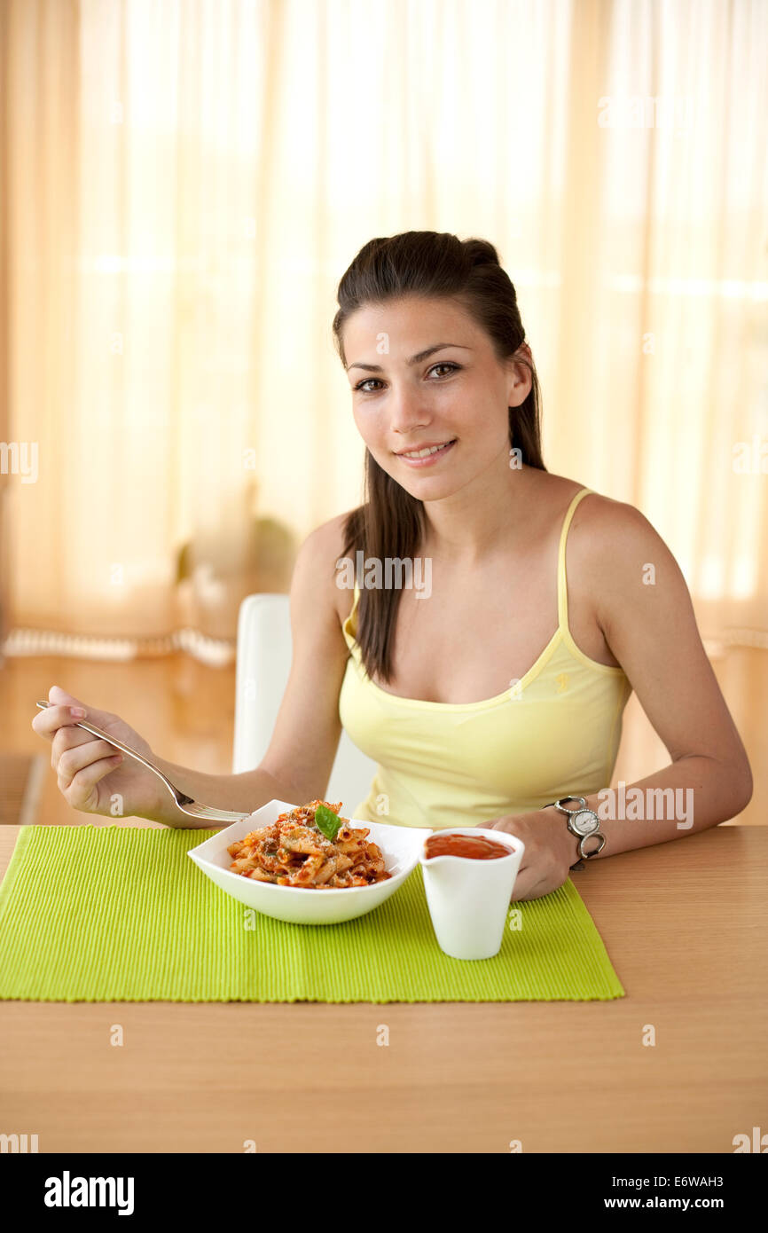 Giovane donna felice di mangiare la pasta italiana con pomodori, parmezan e basilico. Foto Stock