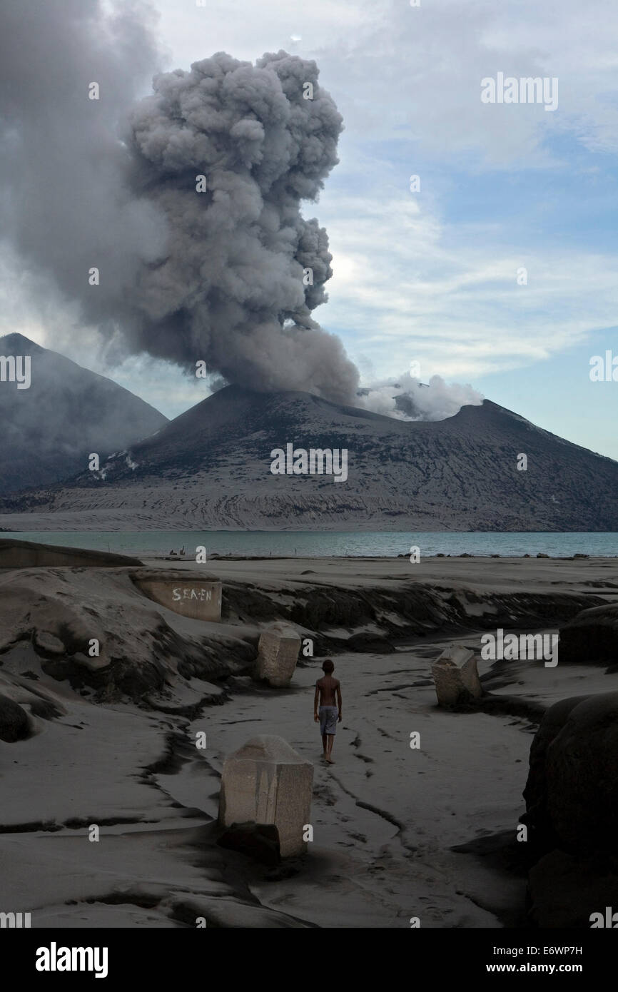 Bambini che giocano tra le rovine di una vecchia fabbrica di cemento con il vulcano in eruzione in background, Vulcano Tavurvur, Rabaul, EA Foto Stock
