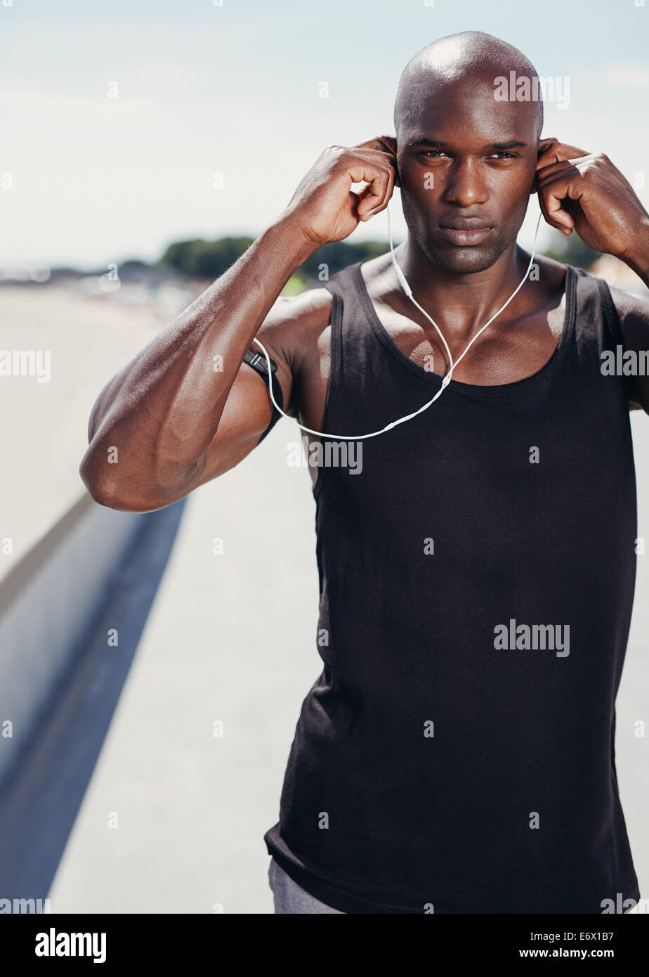 Ritratto di giovane africano che indossa gli auricolari per ascoltare musica. Muscoloso giovane atleta maschio all'esterno. Foto Stock
