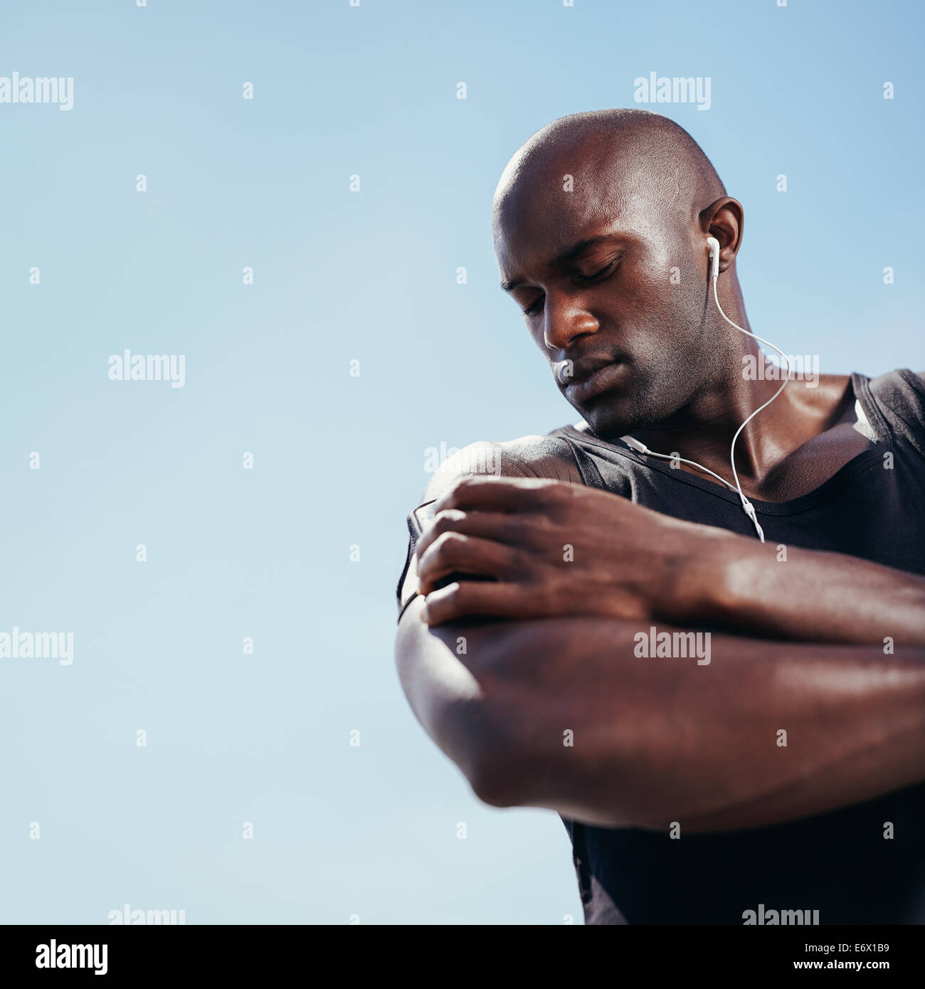 Basso angolo di vista muscolare africana uomo che ascolta la musica sul telefono cellulare. Montare il giovane uomo contro il cielo. Foto Stock