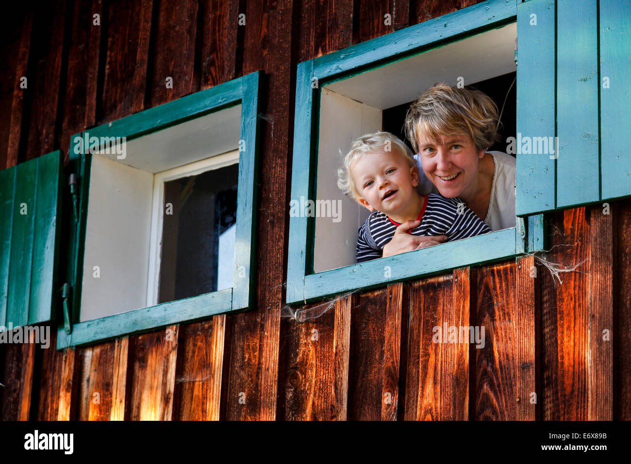 La madre e il figlio di 2 anni) guardando fuori da una finestra di un rifugio alpino, vicino a Maria Alm, del Pinzgau, Salisburgo, Austria Foto Stock