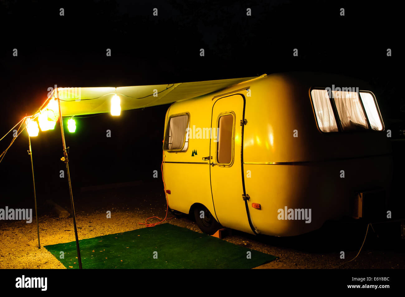 Il picaro travel trailer set up con una tettoia e luci in un campeggio di notte Foto Stock