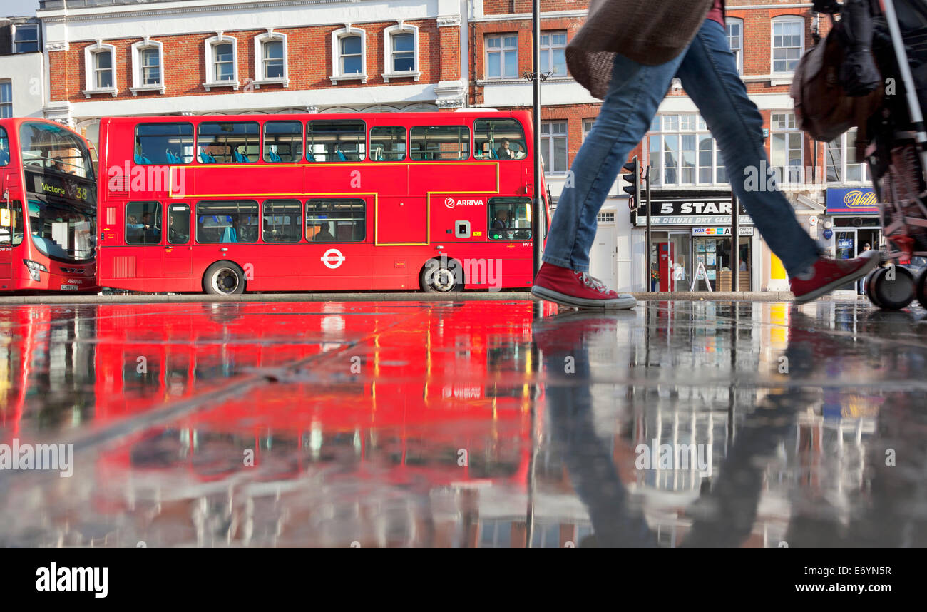 London bus e pedone si riflette nel pavimento bagnato. Foto Stock