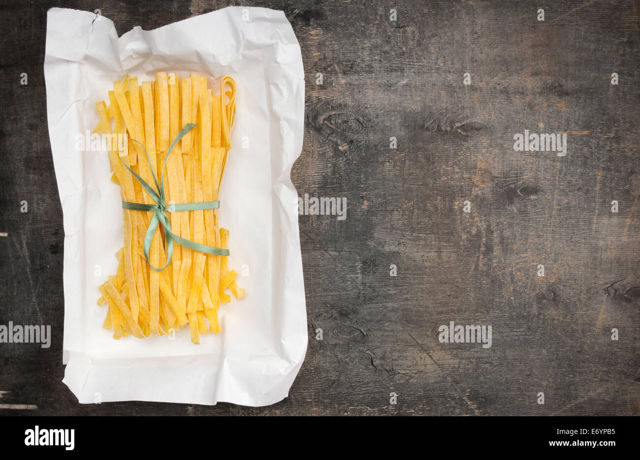 Italian tagliatelle fatte in casa fettuccine in imballaggi di carta con nastro verde sul vecchio tavolo in legno Foto Stock