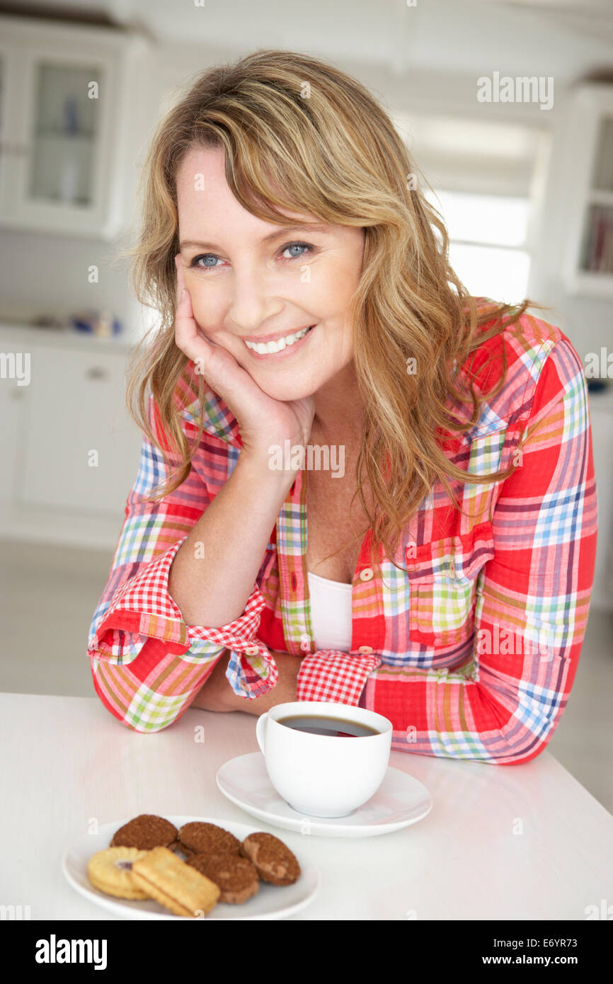 Metà donna età con caffè e biscotti a casa Foto Stock