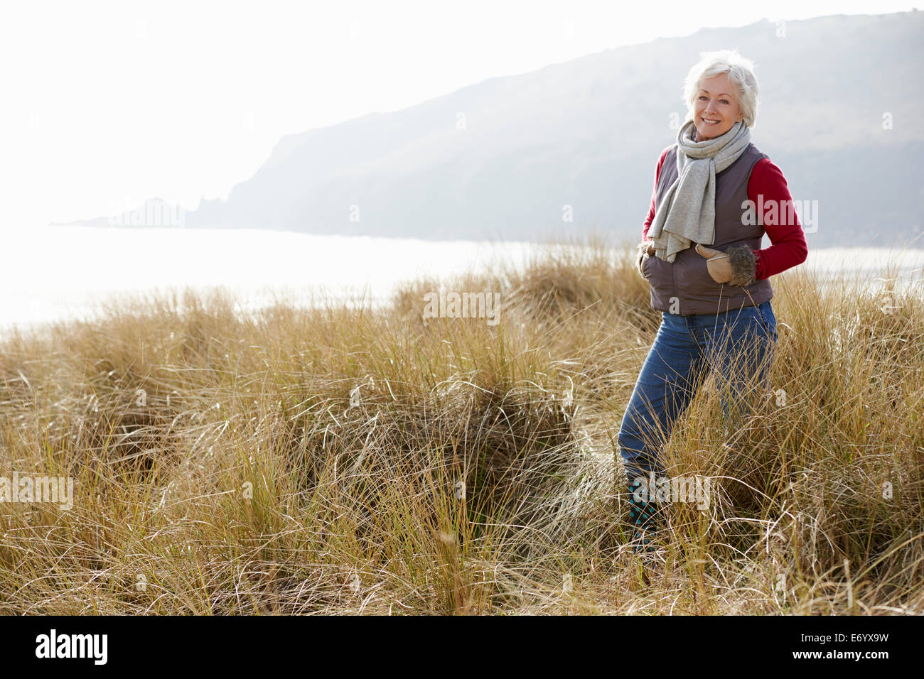Senior donna a piedi attraverso le dune di sabbia sulla Spiaggia Invernale Foto Stock