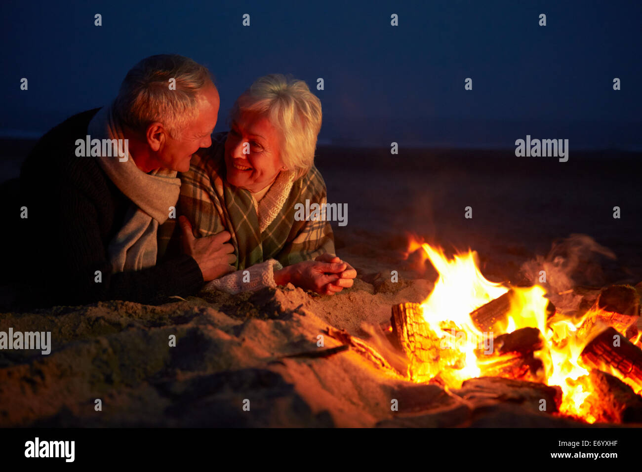 Coppia senior seduti davanti al fuoco sulla Spiaggia Invernale Foto Stock