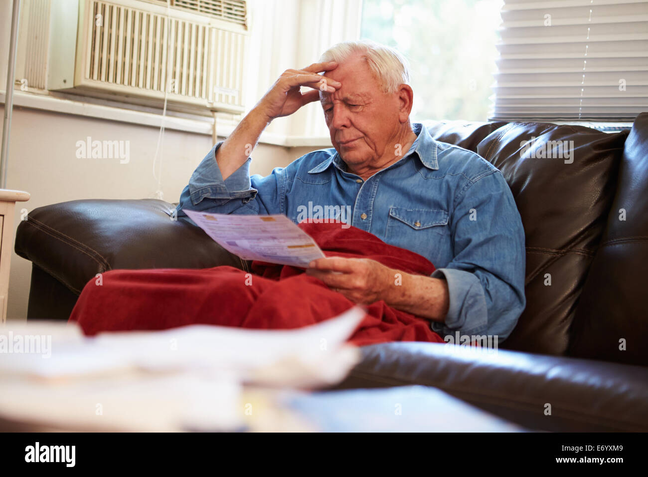 Preoccupato Senior uomo seduto sul divano guardando le bollette Foto Stock