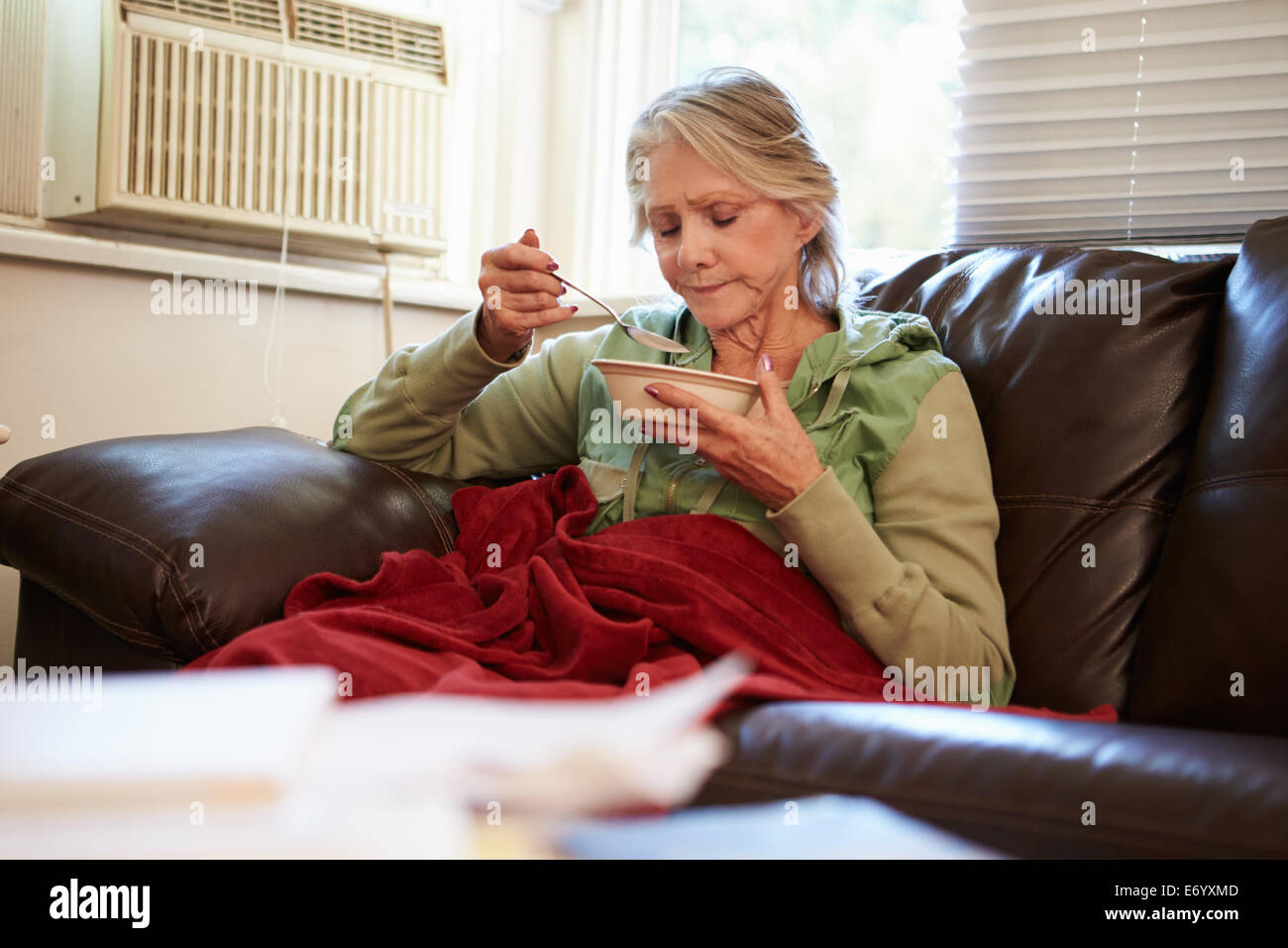 Senior donna con dieta povera di mantenere caldo sotto coperta Foto Stock